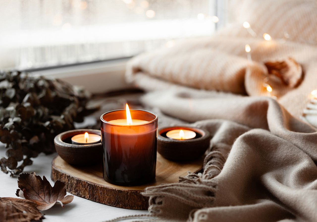 A cozy scene featuring candles and a soft blanket on a table beside a window, creating a warm atmosphere.