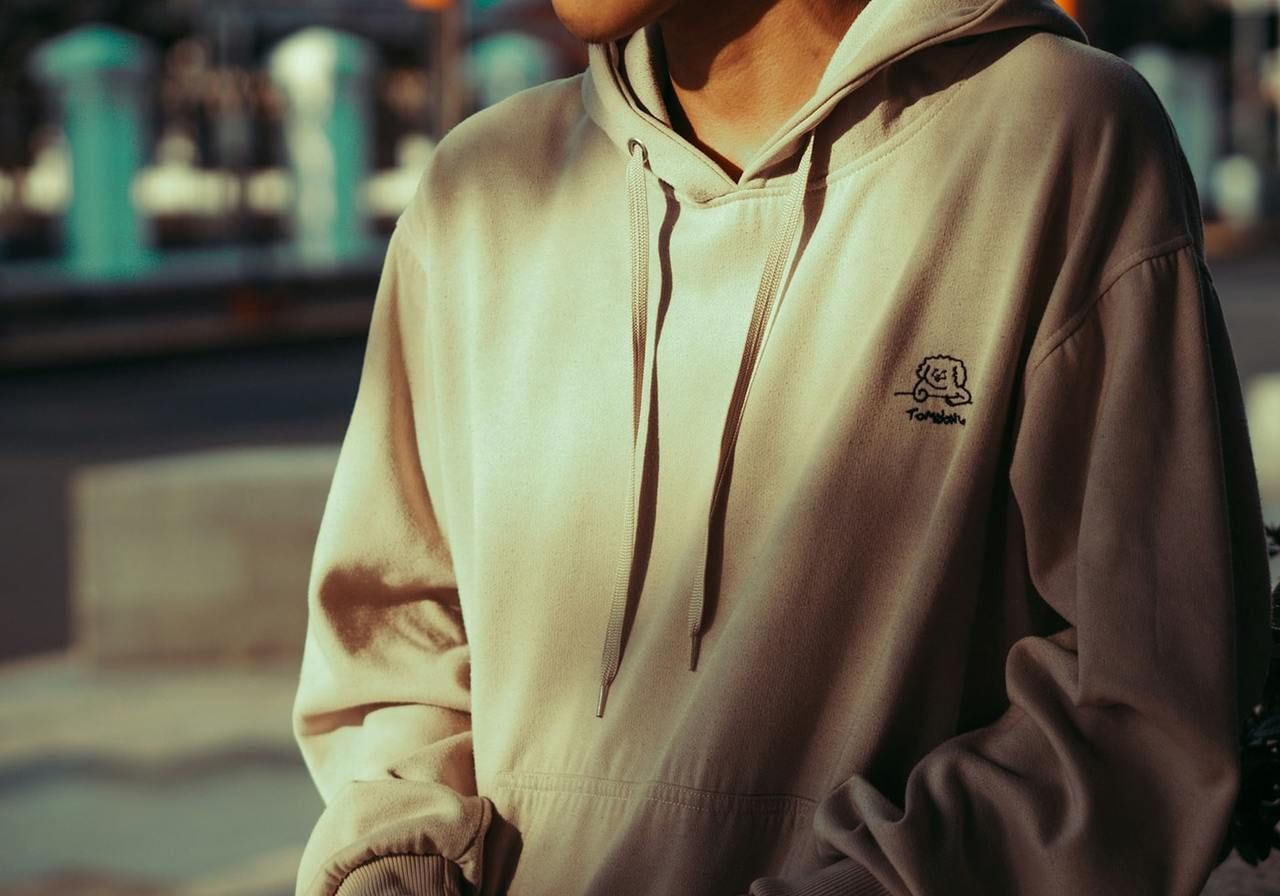 A person in a light hoodie with an embroidered image on the left chest area.
