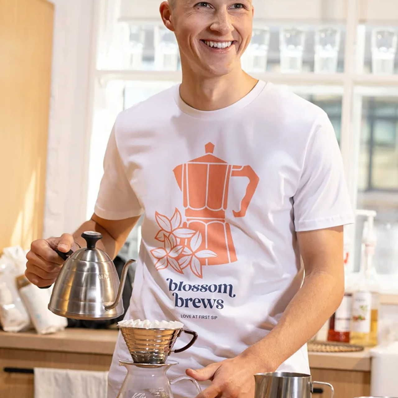 A man wearing a white Unisex Organic Cotton T-Shirt | Stanley/Stella STTU169 with a coffee-themed print in orange.