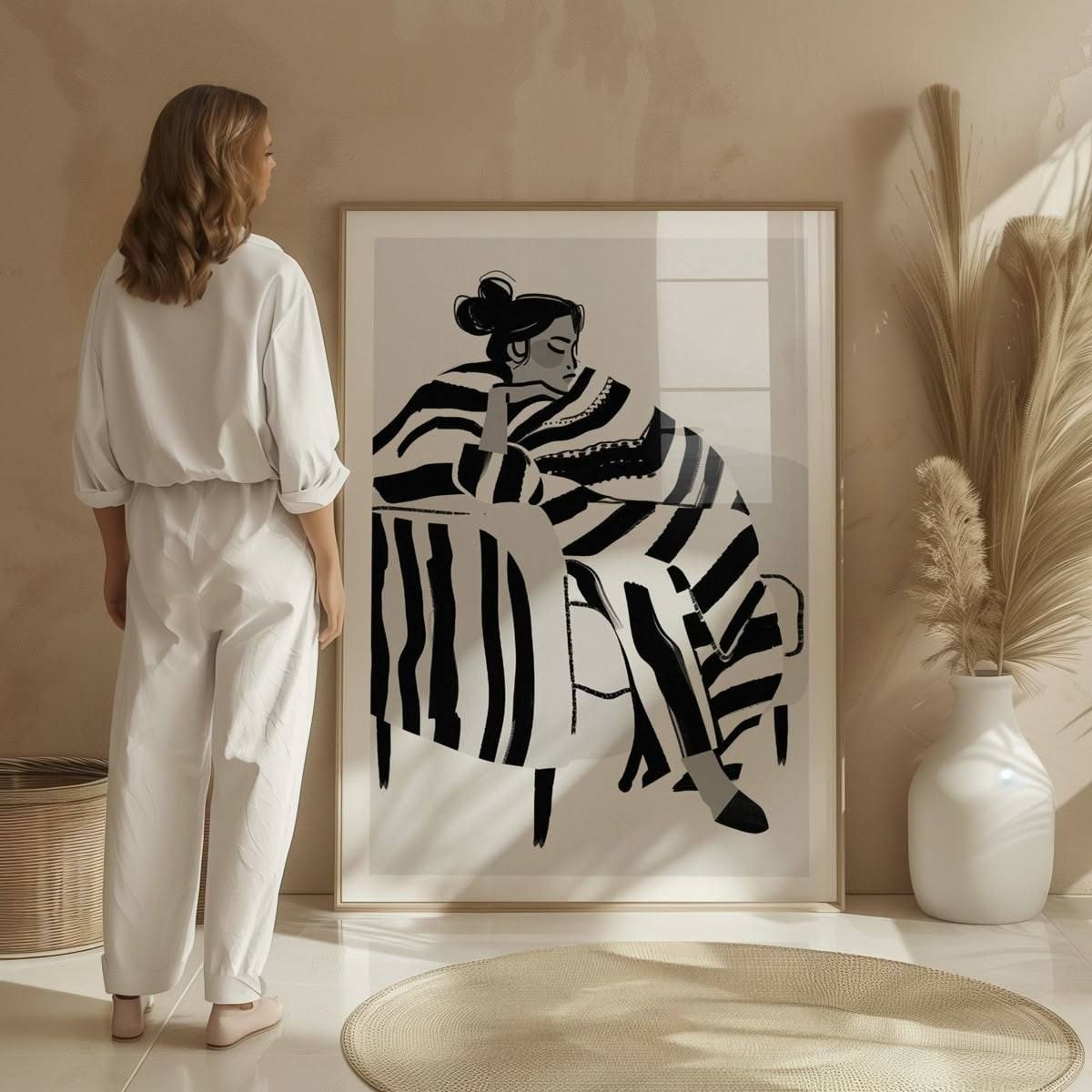 A woman in white pajamas stands before a large black and white print, showcasing her relaxed demeanor and artistic surroundings.