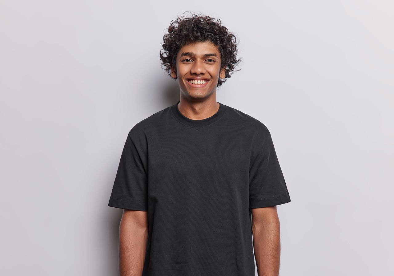 Smiling man wearing a plain black t-shirt against a plain gray background.