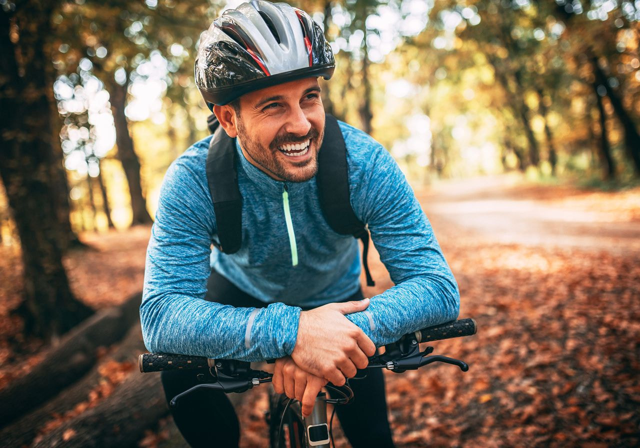 A man smiles joyfully while riding his bike through a lush green forest.
