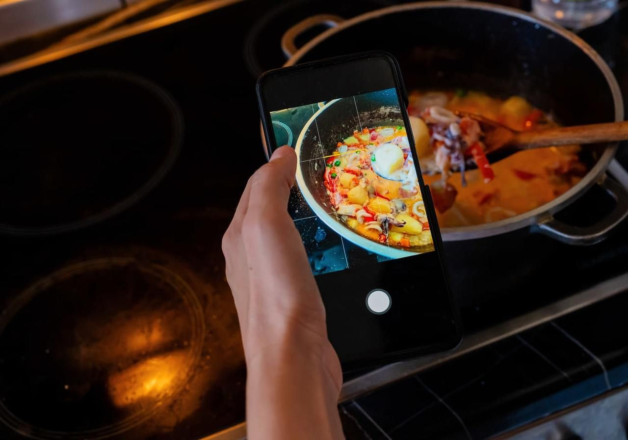 A man is filming a dish being cooked using a mobile phone.