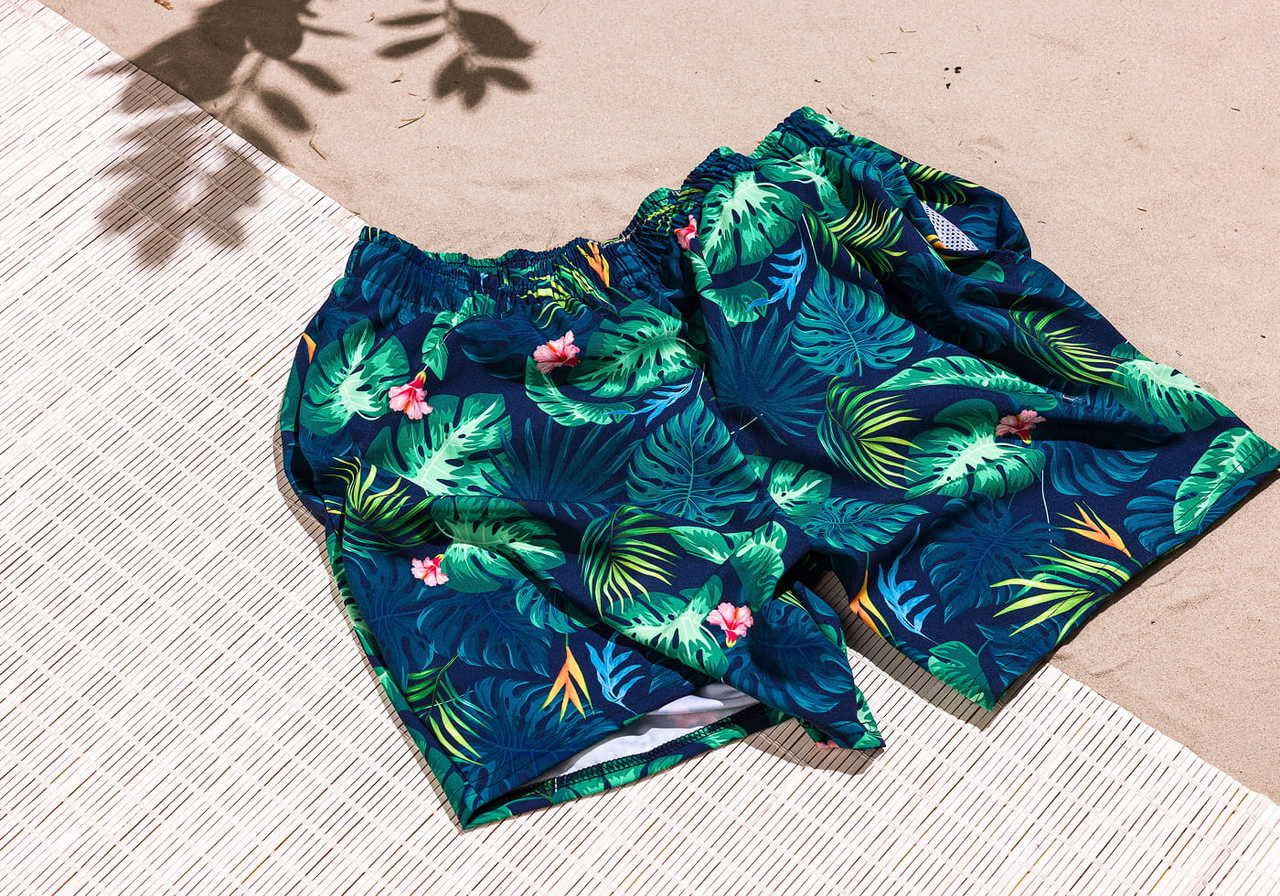 A pair of tropical print swim trunks lying on a sandy surface.
