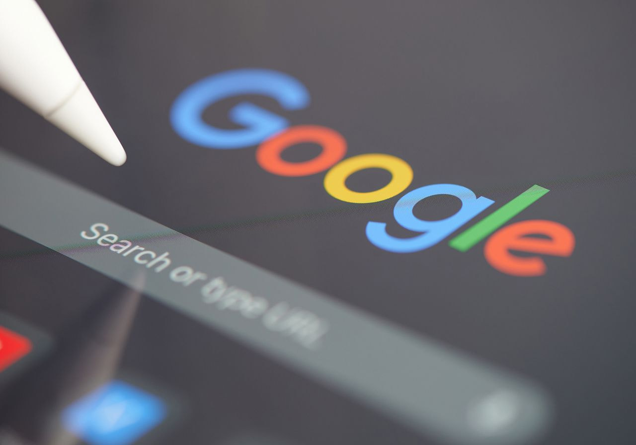 A stylus points to a digital screen displaying the Google logo above a search bar. 