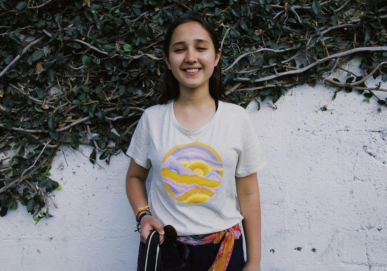 A smiling young woman wearing a custom white t-shirt with an abstract sun illustration print on the front.