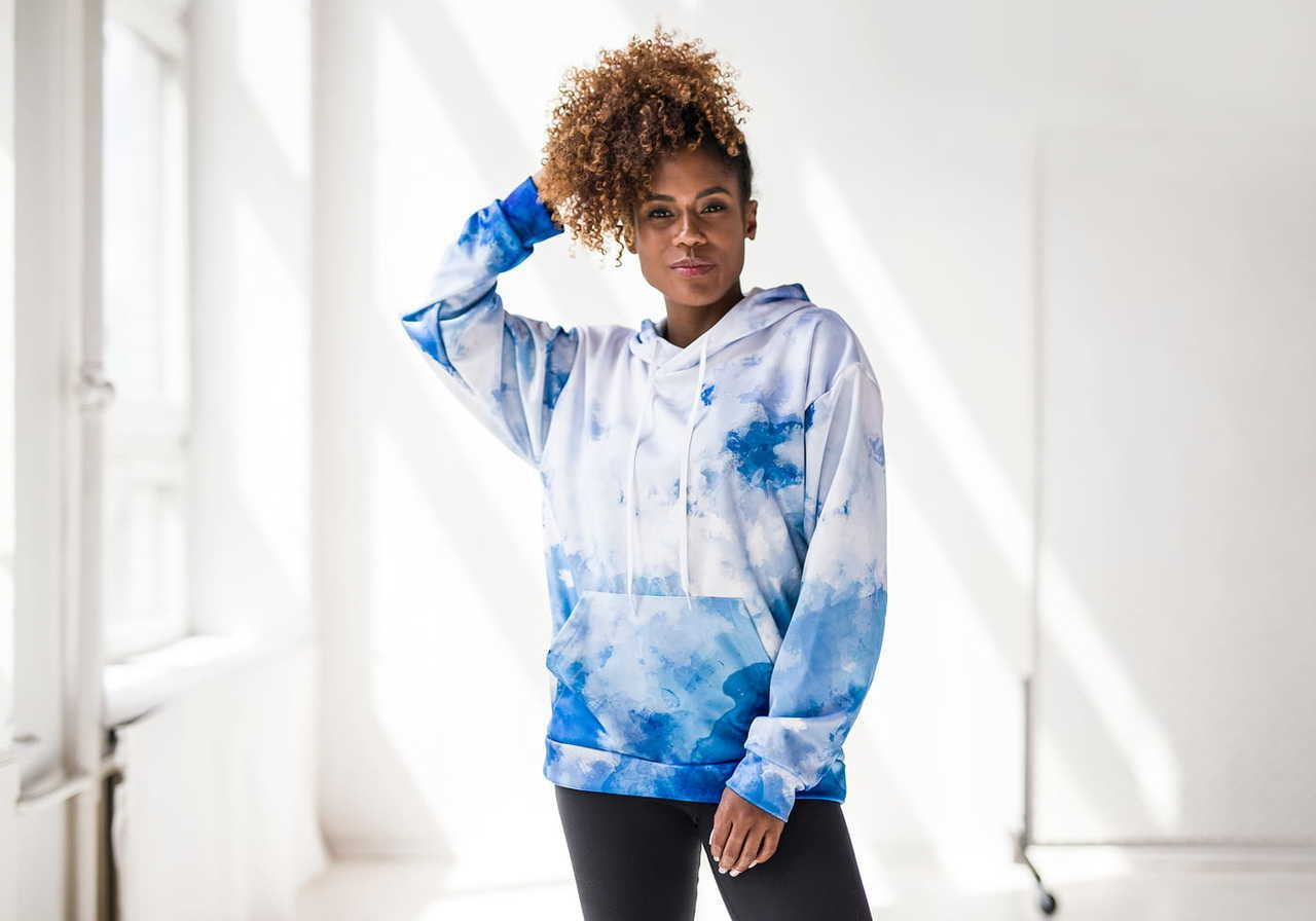 A woman wearing a blue and white tie-dye hoodie, standing in a bright, well-lit room.