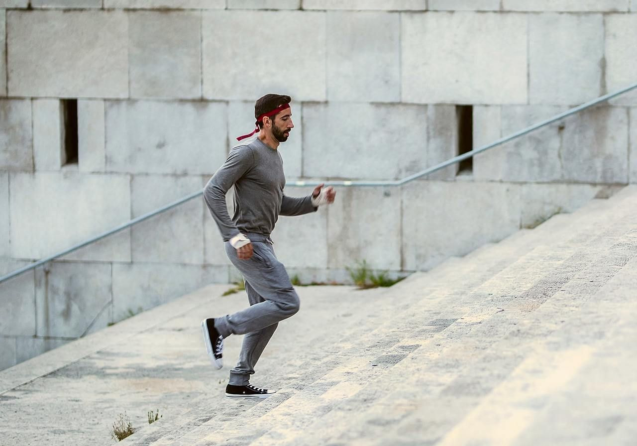 A man in athletic wear with a red headband runs up a stone staircase.