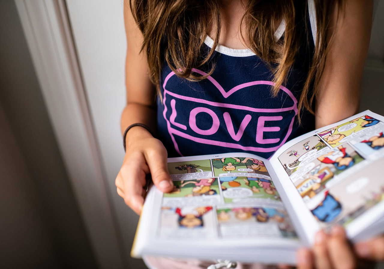 A person holding a comic book while wearing a tank top with the word "LOVE" on it.