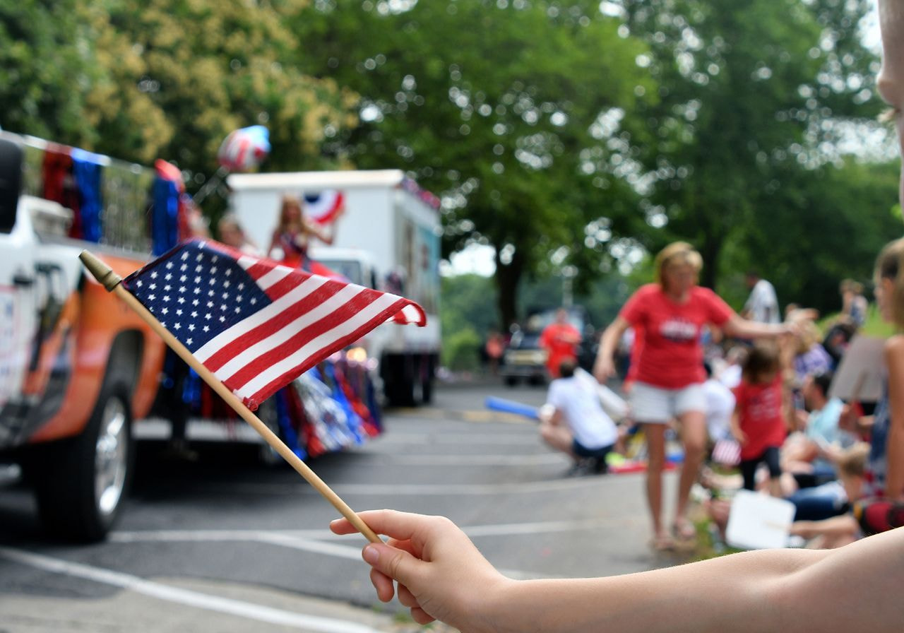 A person proudly holds an American flag while standing in front of a festive parade.