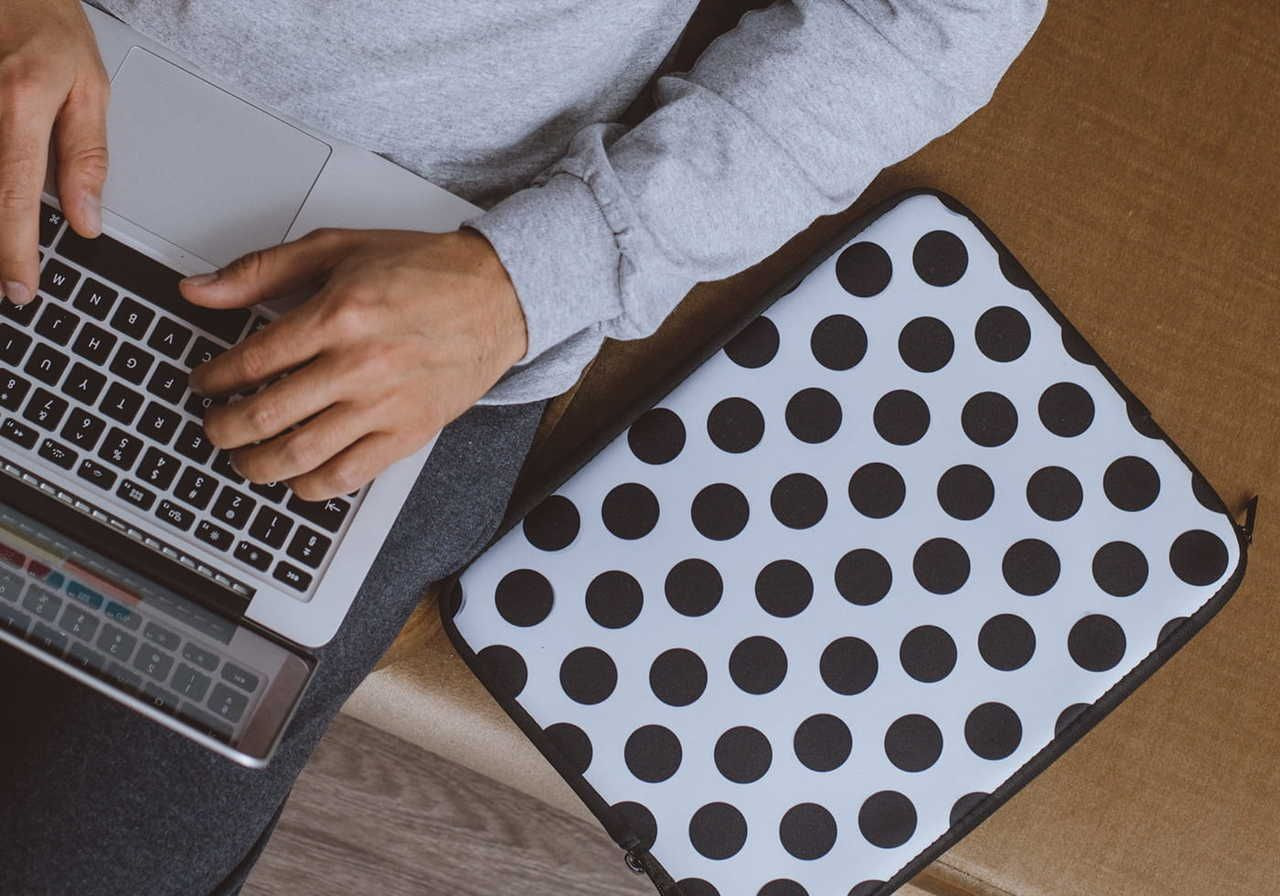 A person typing on a laptop with a polka dot laptop case nearby.