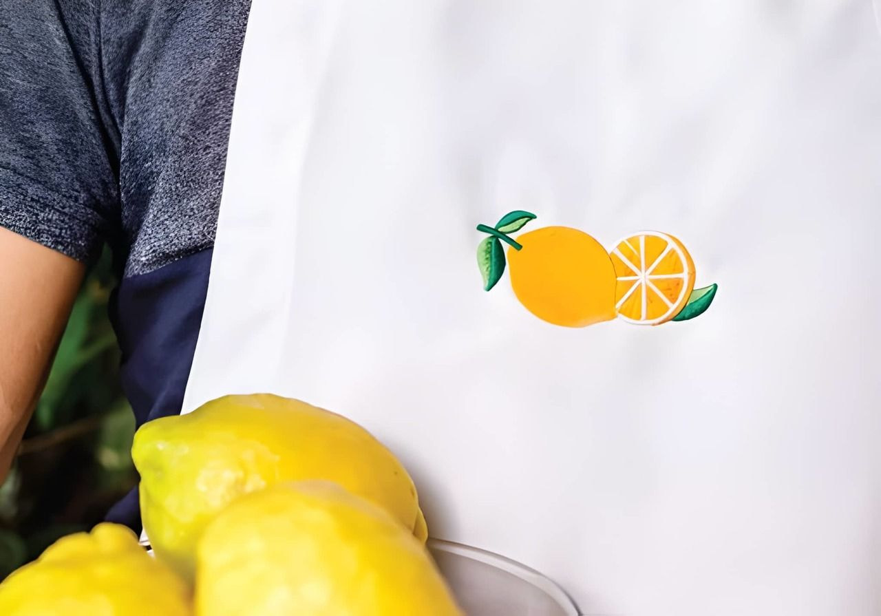 A person holding lemons in a white apron with a pair of lemons embroidered.