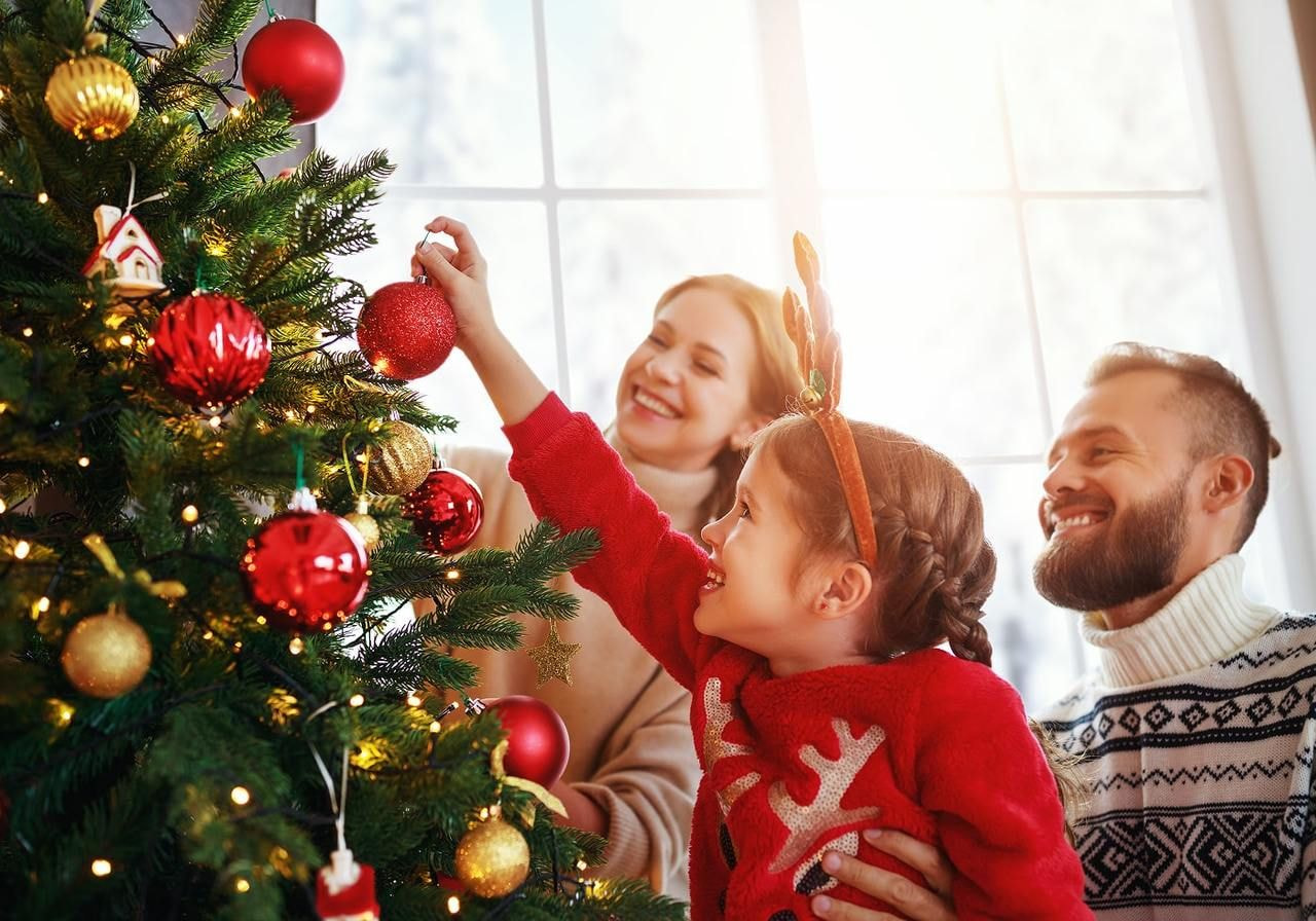 A family joyfully decorating a Christmas tree with colorful ornaments and lights in a cozy living room setting.