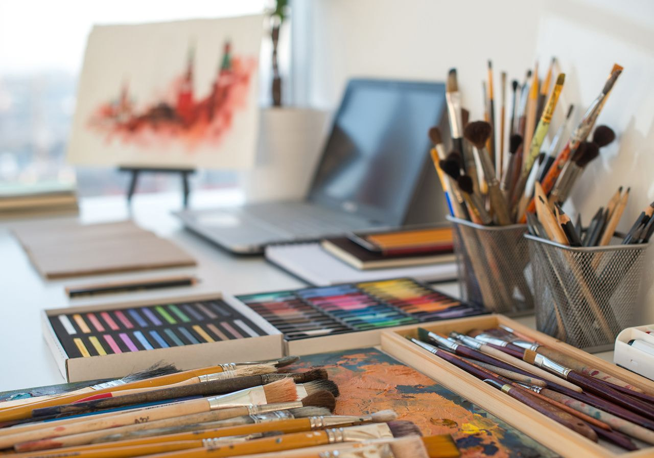 A desk featuring a laptop and a collection of paintbrushes arranged neatly beside it.