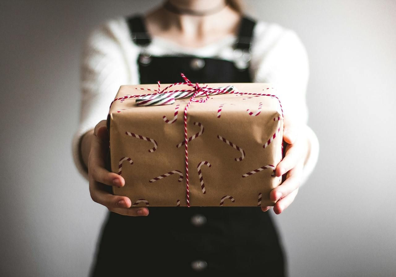 A woman smiling while holding a beautifully wrapped gift box in her hands.