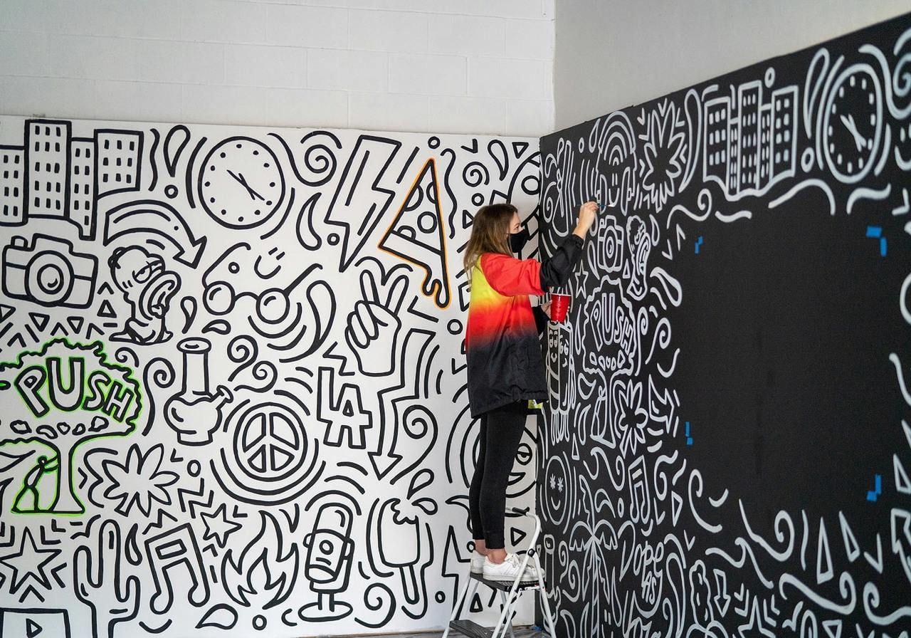 A woman is applying colorful graffiti to a wall, showcasing her artistic expression and creativity.