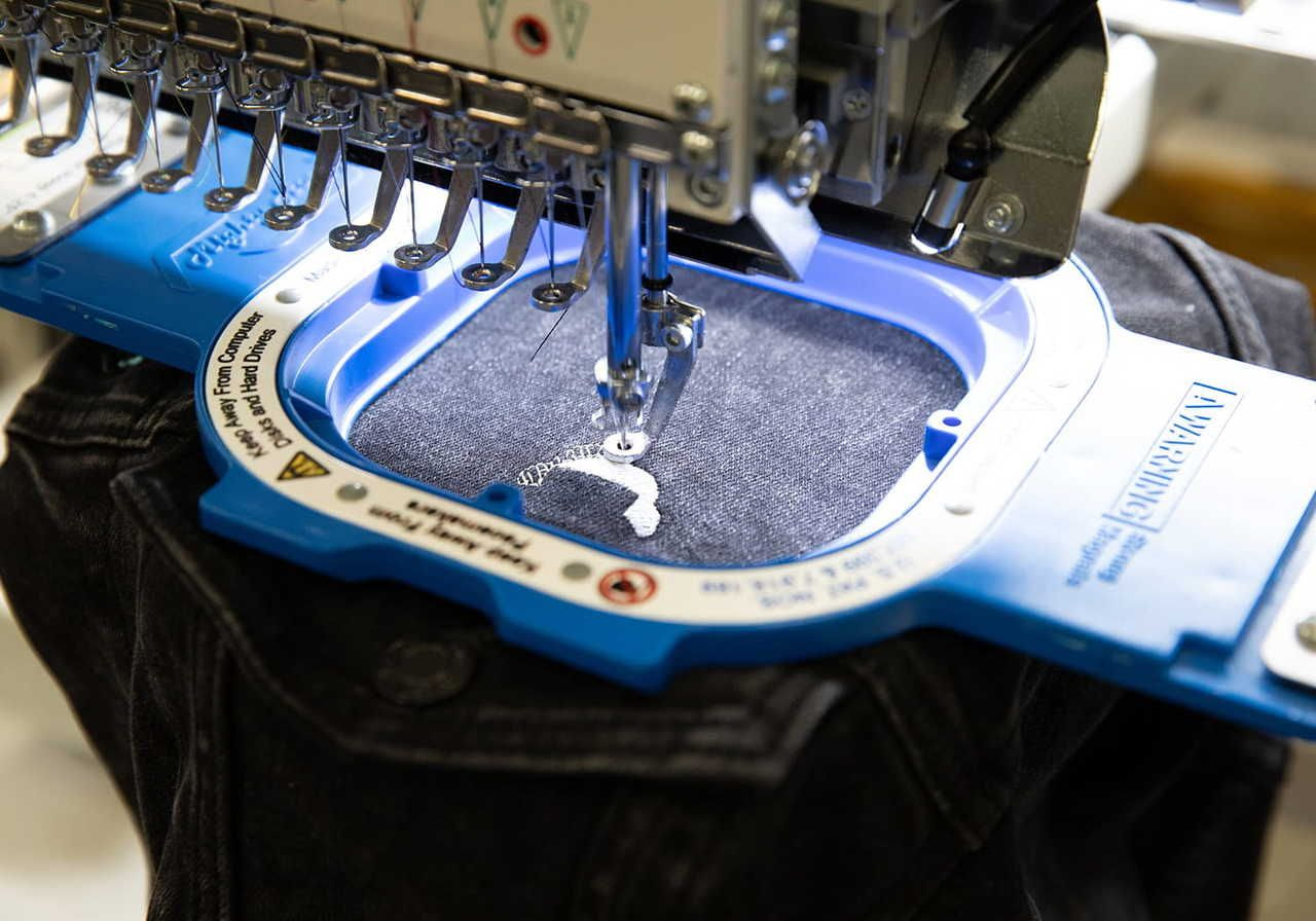 An embroidery machine stitching a design onto black fabric.