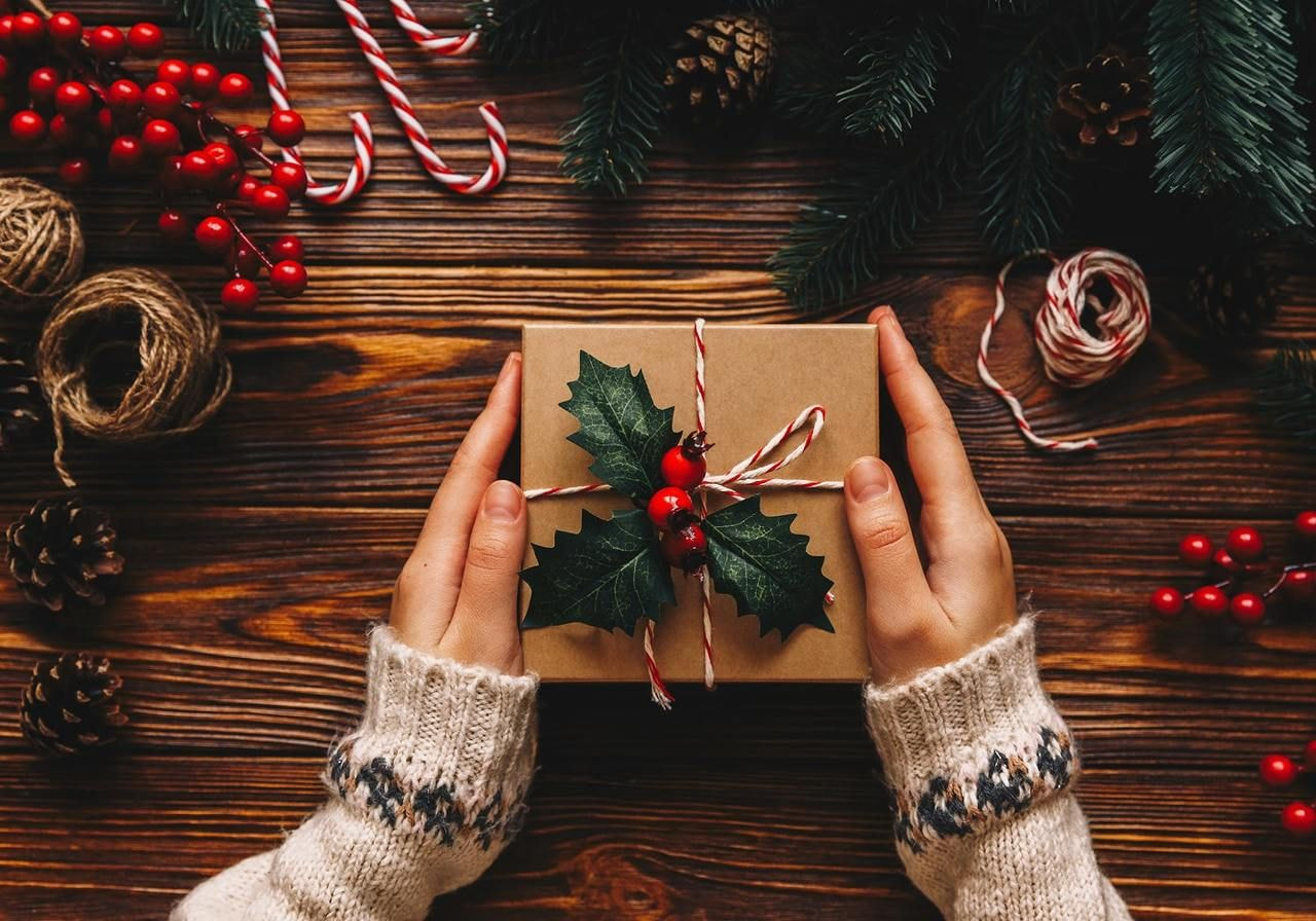 Woman's hands holding a wrapped gift box on a rustic wooden table.