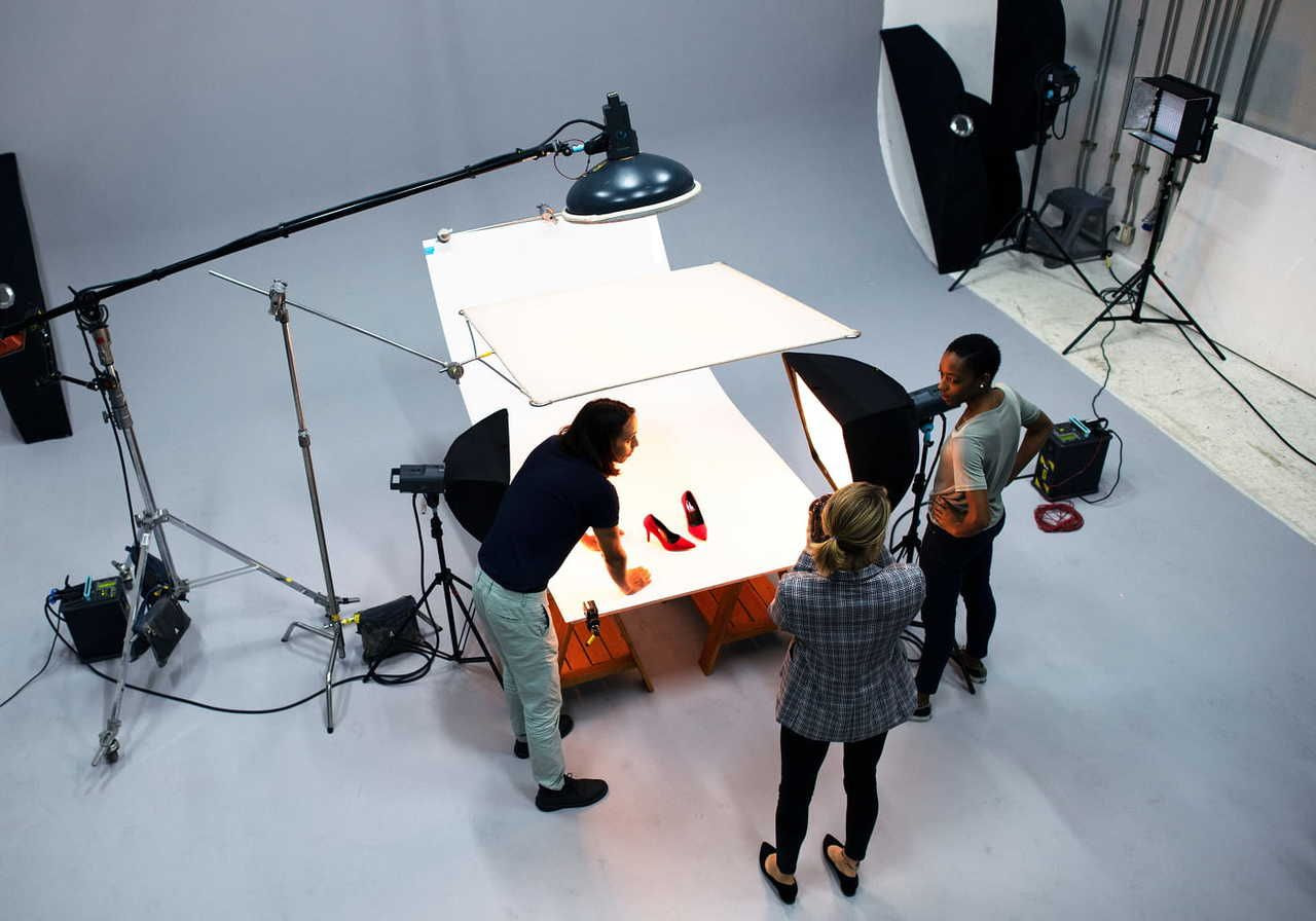 Overhead view of a photo studio with three people around a lighted table, photographing a product.
