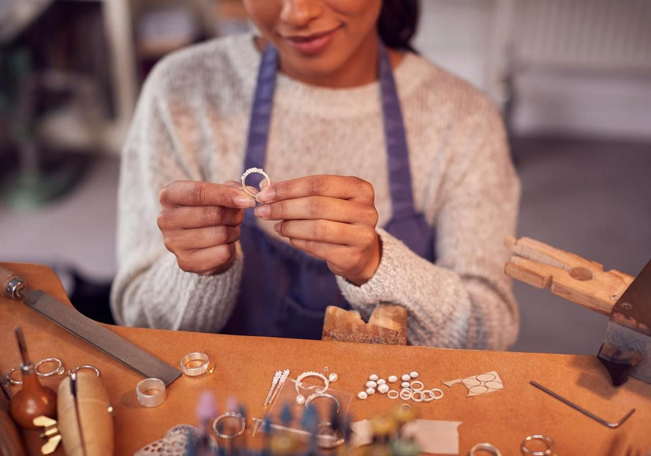 A woman is crafting a ring in her workshop, surrounded by tools and materials for jewelry making.