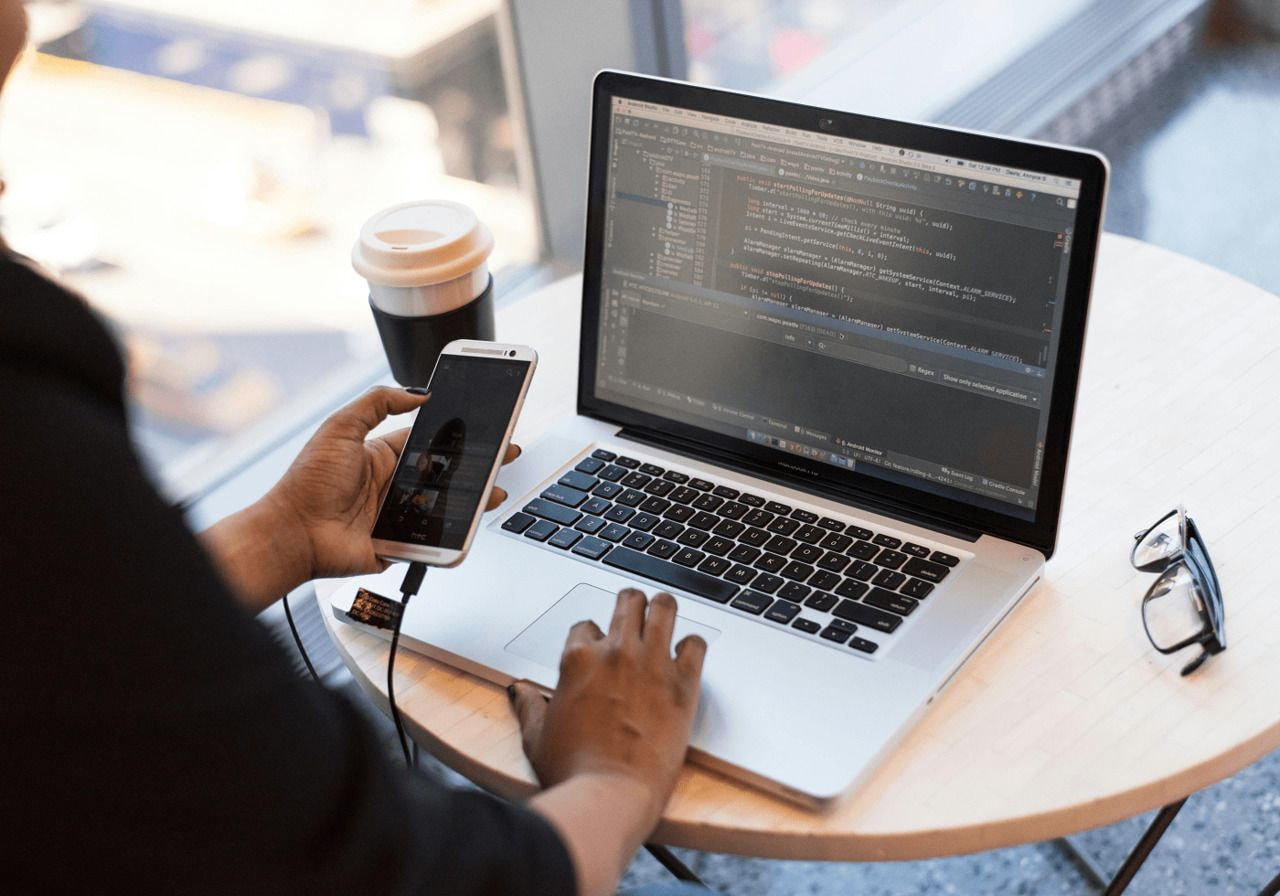 A person coding on a laptop against a plain white background, focused on their work.