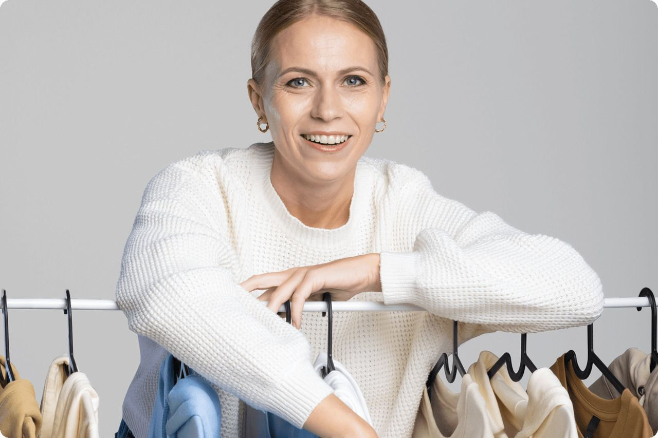 A smiling woman holds a rack of colorful clothes, showcasing her enthusiasm for fashion and style.