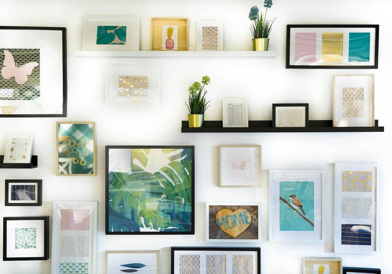 A wall adorned with various framed pictures and lush green plants, creating a vibrant and artistic atmosphere.