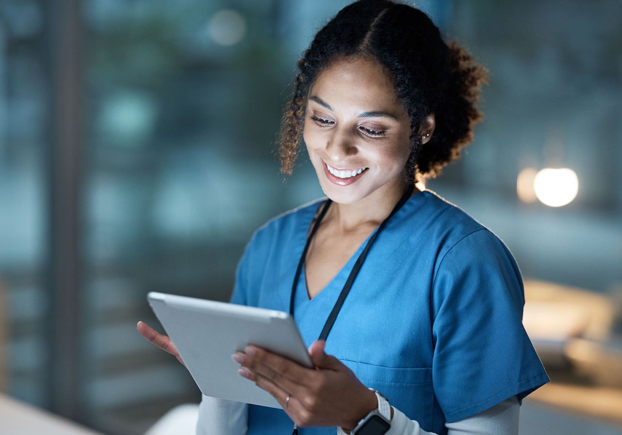 A woman in medical scrubs is focused on using a tablet, likely for patient care or medical information.
