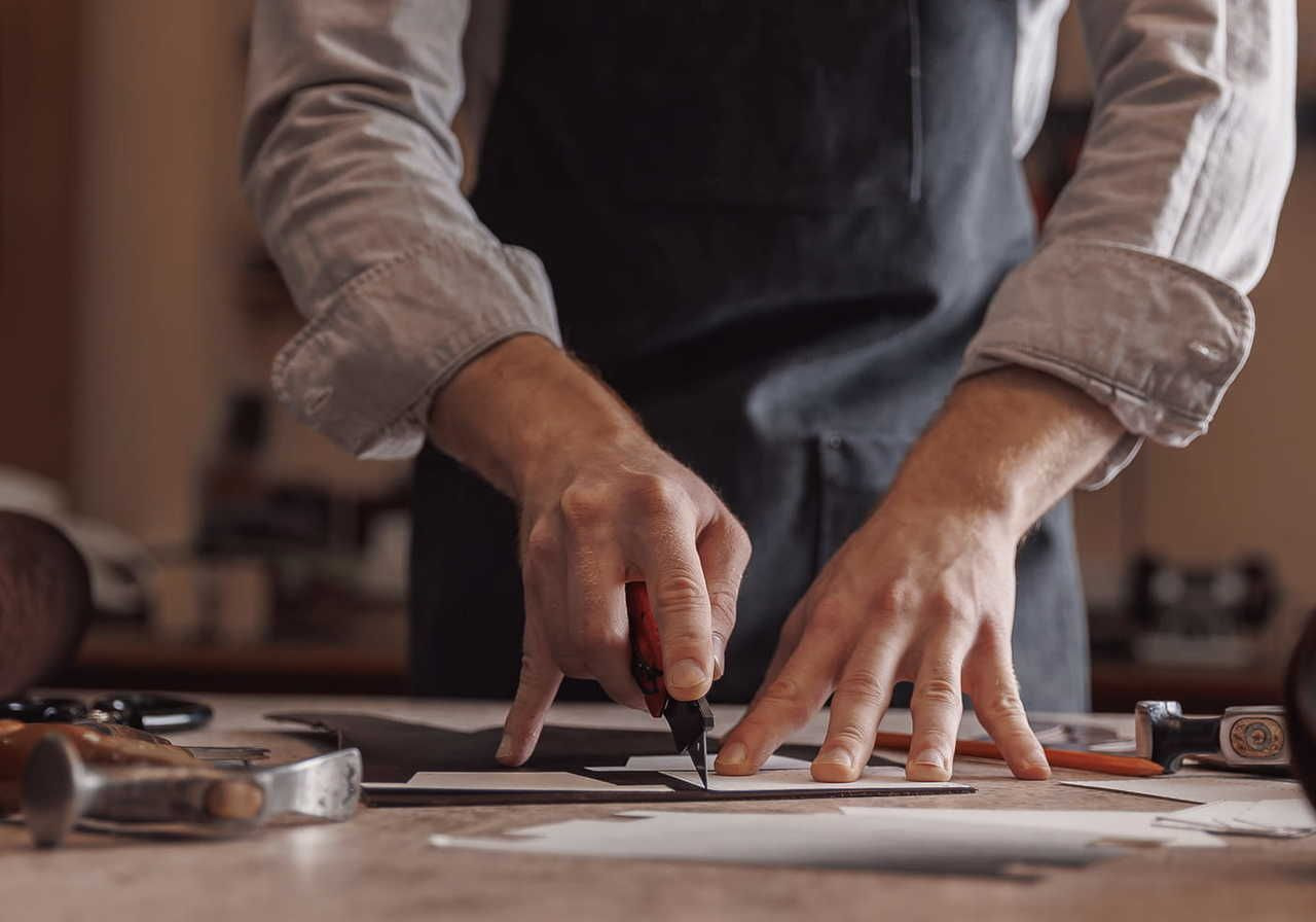 Man’s hands cutting through a piece of leather.