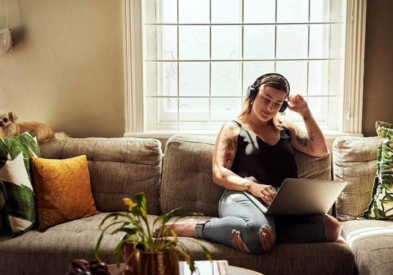 A woman with headphones sits relaxed on a sofa, using a laptop, learning how to make money on Twitch.
