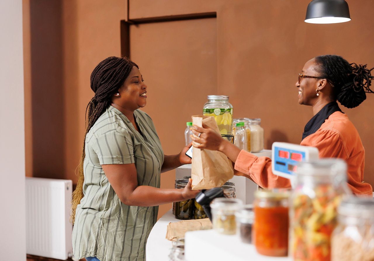 Two women standing at a counter, smiling while preparing and serving food together.