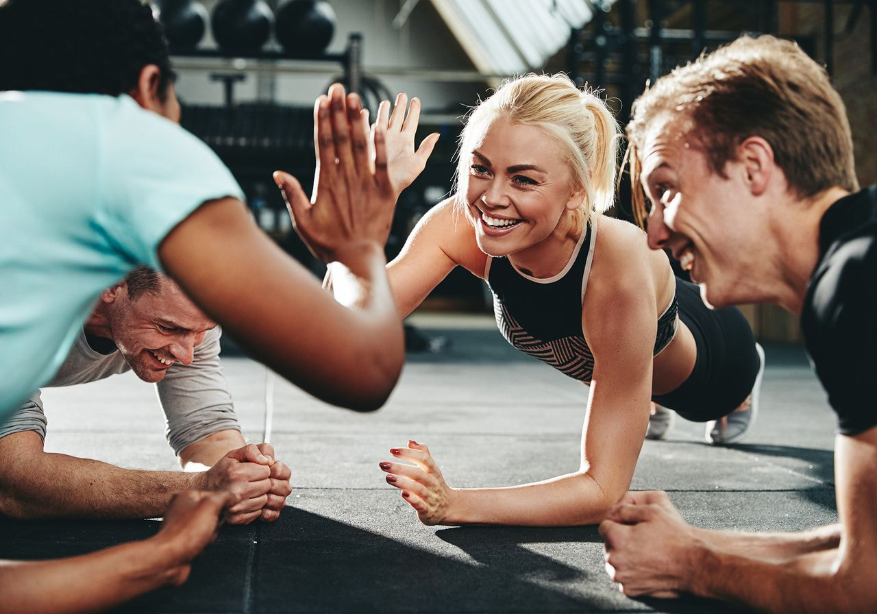 A group of five individuals performing push-ups in a gym setting, demonstrating teamwork and fitness.