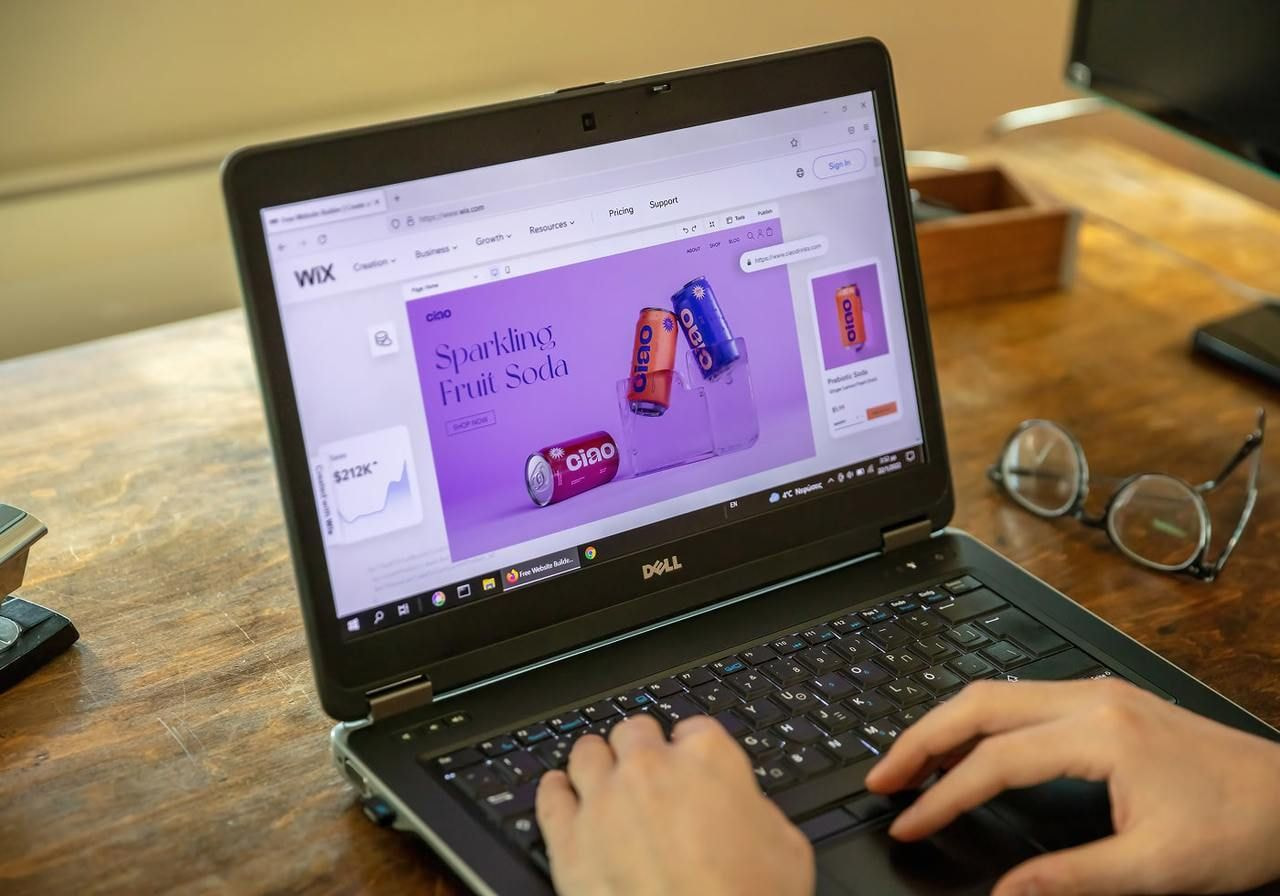 A person is using a laptop while seated at a desk. The Wix website builder is on the screen.
