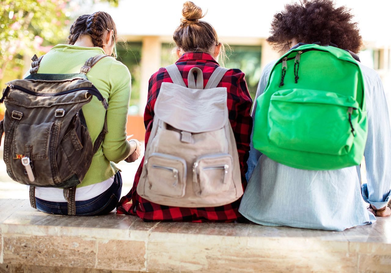 A group of kids sitting with their backpacks on.