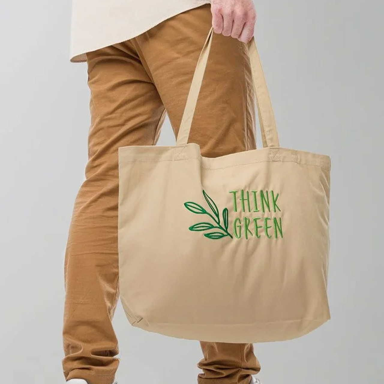 Person in tan pants holding a beige tote bag with an embroidered