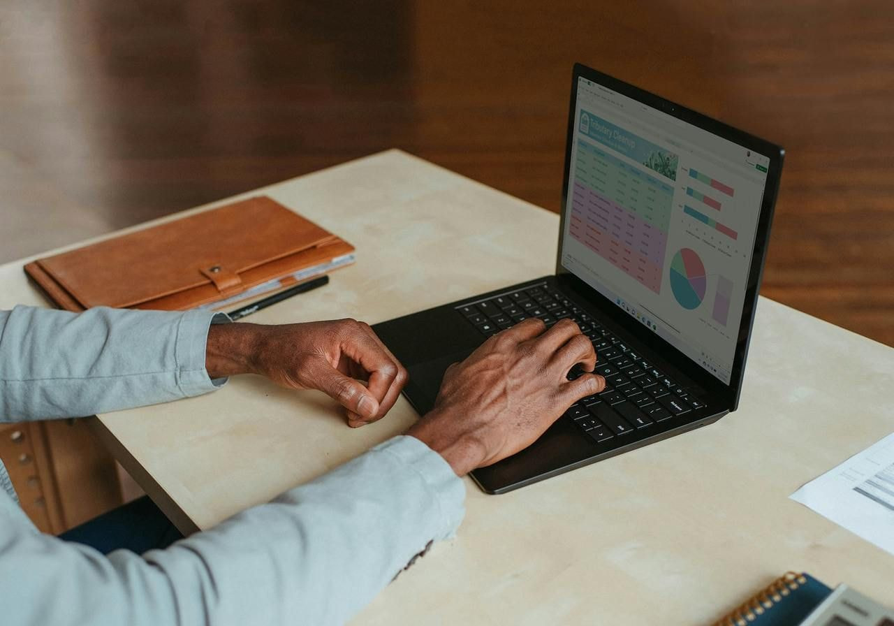 Man focused on a laptop while sitting at a desk, surrounded by office supplies and a plant.
