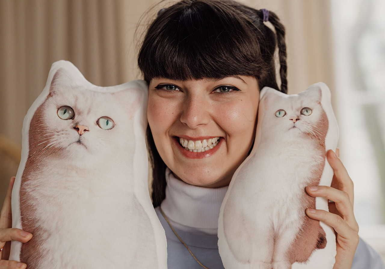 A young woman smiling while holding two cat-shaped pillows made with sublimation printing.