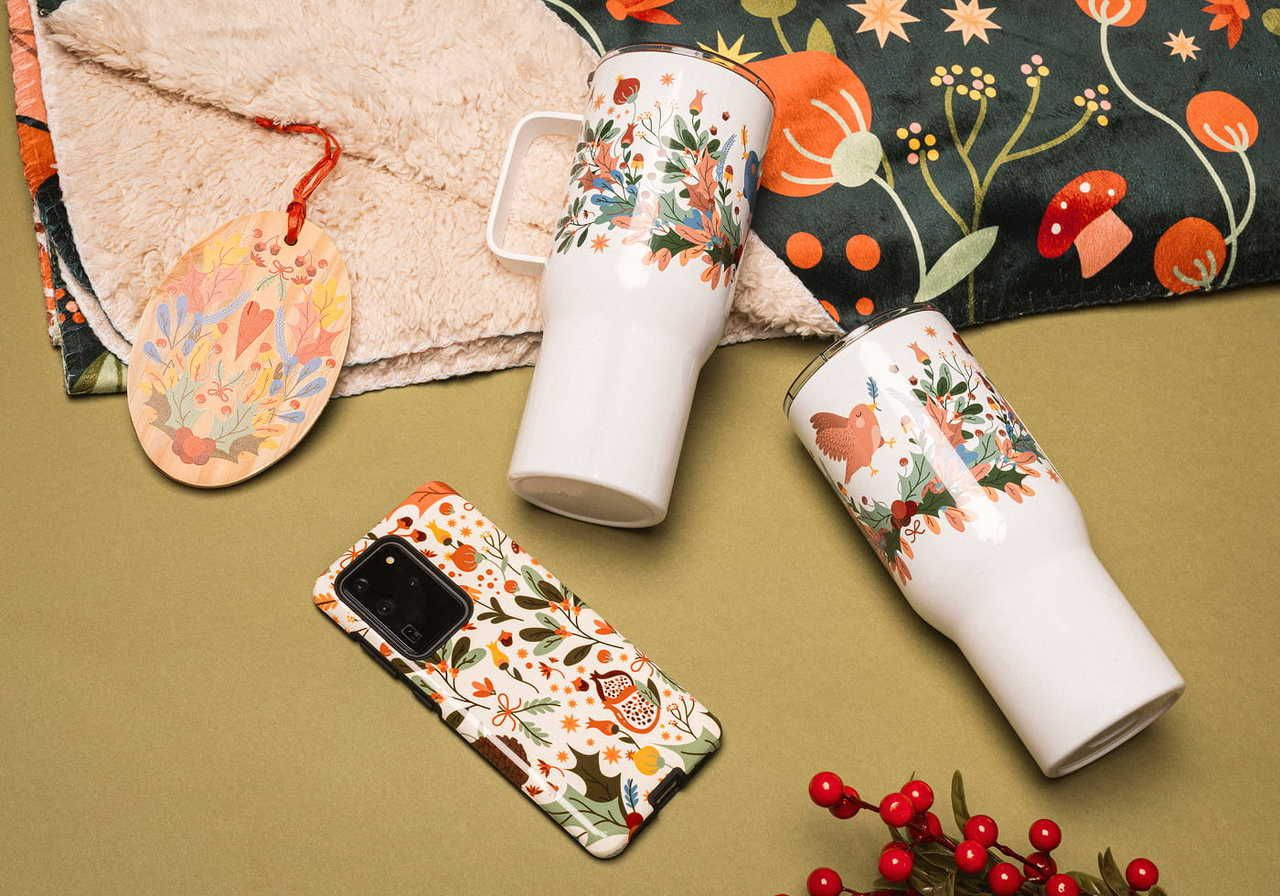 A flat lay arrangement featuring two decorative mugs, a patterned cloth, a tag, and a smartphone in a case with floral designs.