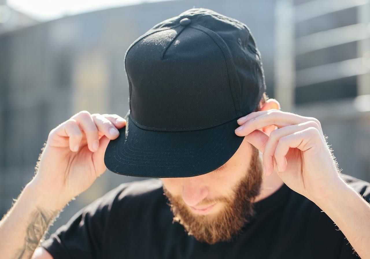 A man is putting on a black 5-panel hat.