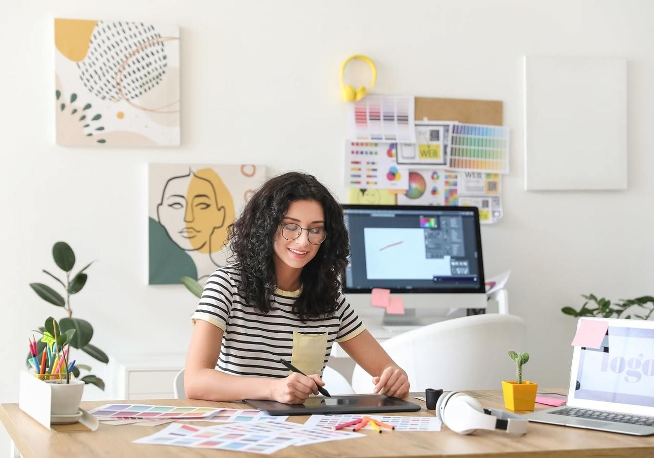 A smiling woman is sitting at a desk and using a pad to create greeting card designs.