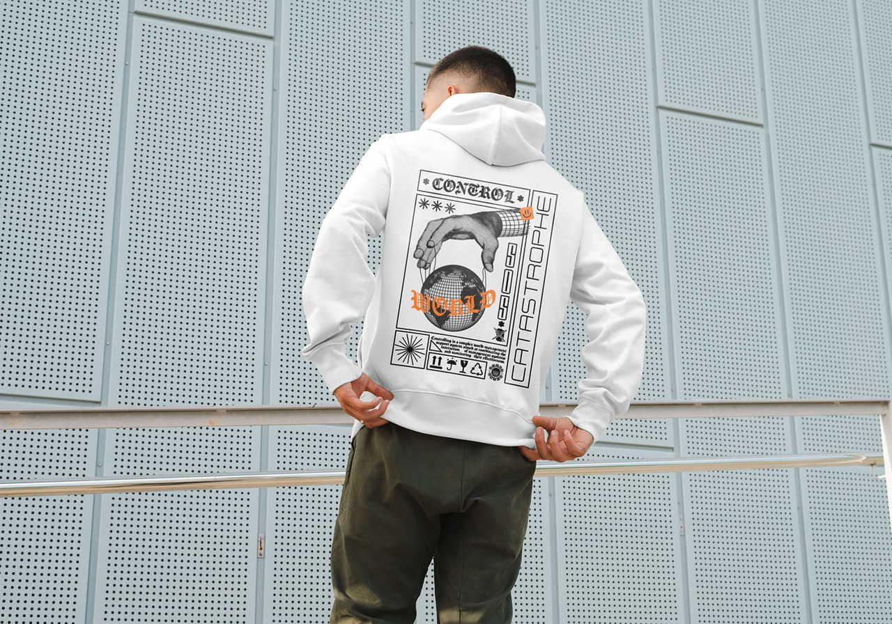 A man wearing a white hoodie with a detailed graphic on the back, featuring a hand holding a globe, abstract designs, and bold text.