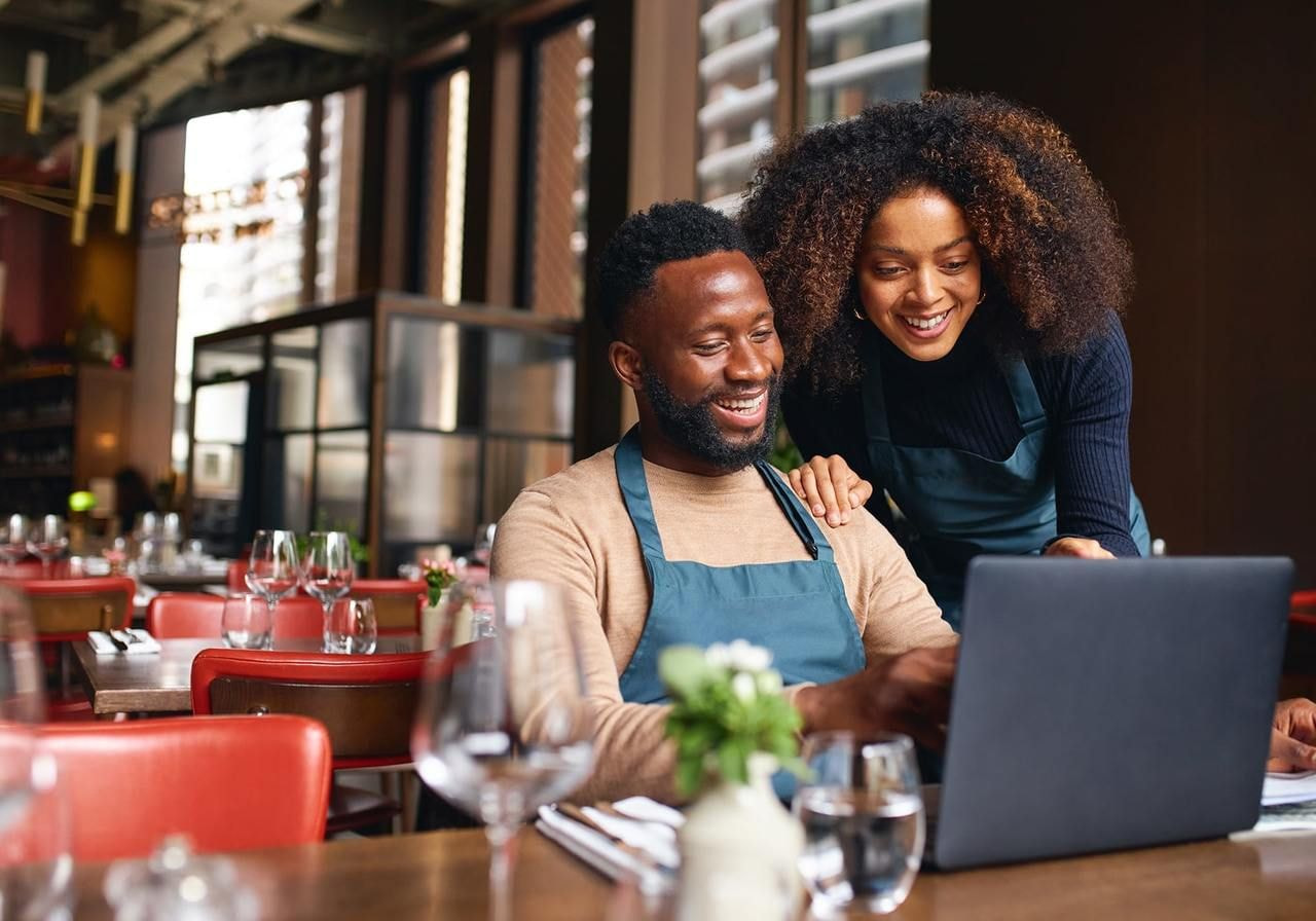 A man and woman smile while working together on a laptop, showcasing a collaborative and positive atmosphere.