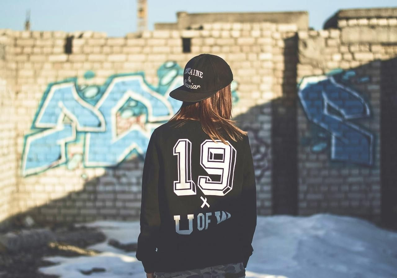 A woman is wearing college merch: a black hoodie with a large “19” print on the back.