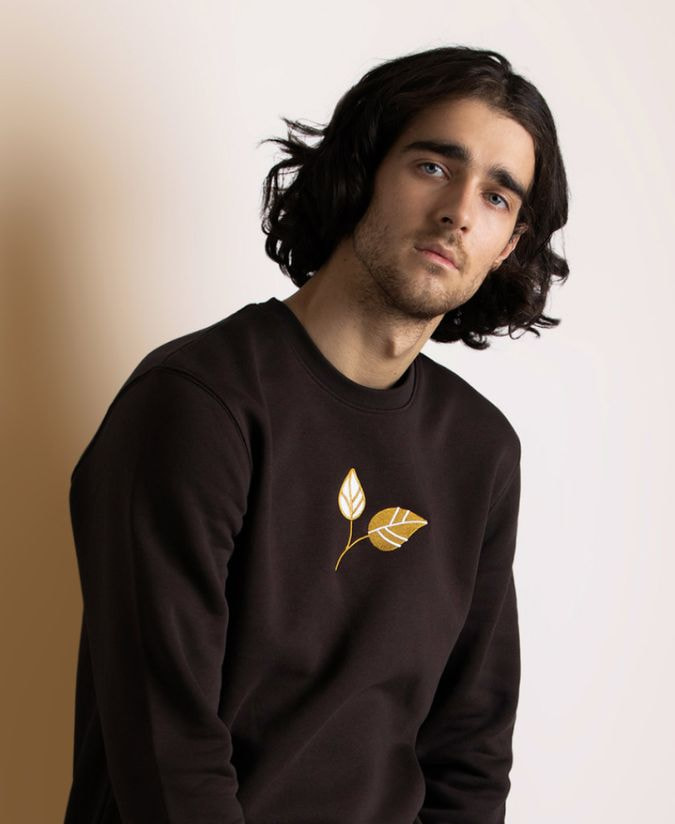 a man wearing a black sweatshirt with embroidered leaves