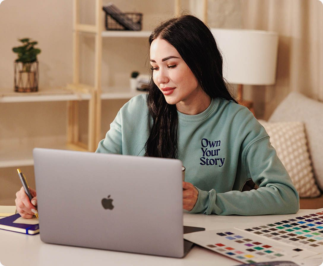 Woman working on laptop while planning clothing designs and color palette samples.