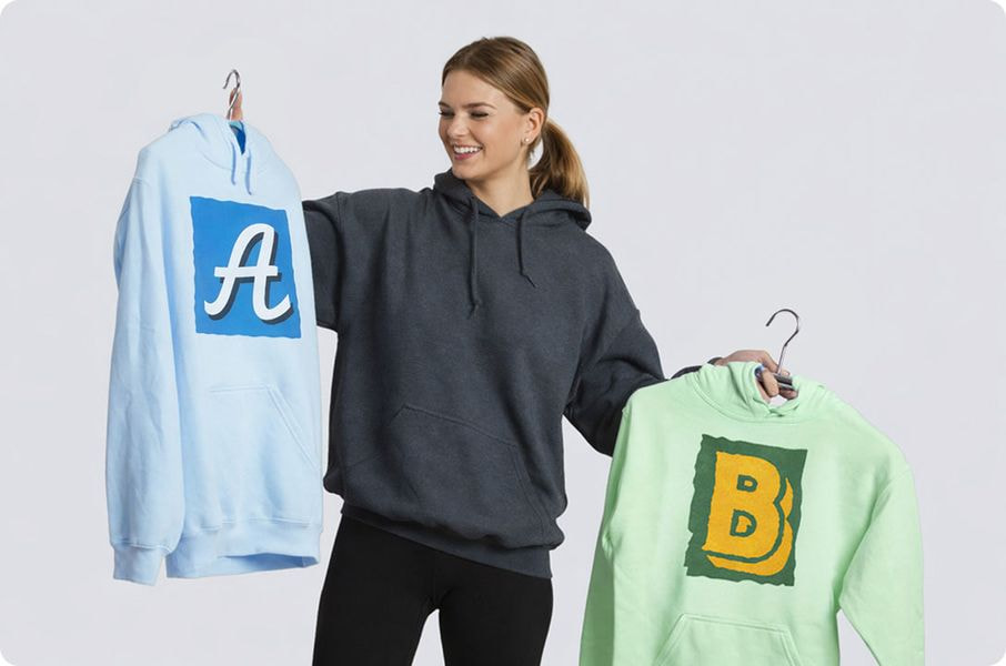 Woman comparing two custom printed hoodies on hangers in a print-on-demand product comparison.