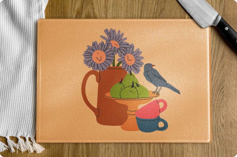 Finished custom cutting board with illustrated design of flowers, fruit, and a bird on a wooden surface.