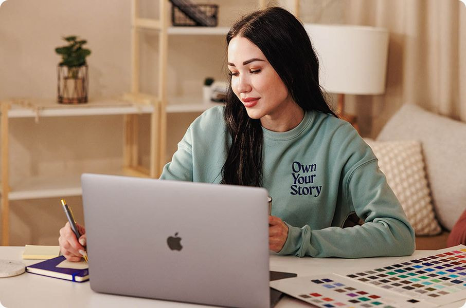 Person working on a laptop while reviewing color swatches, representing the process of creating and selling custom-designed doormats online.