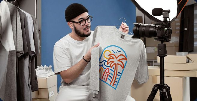 a man holding a custom printed grey t-shirt in front of a camera