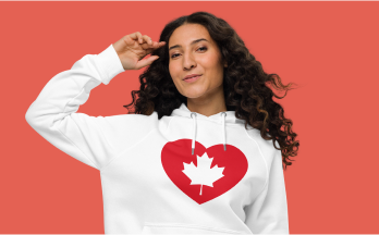a woman with long curly hair wearing a white sweatshirt with a heart and a maple leaf on it